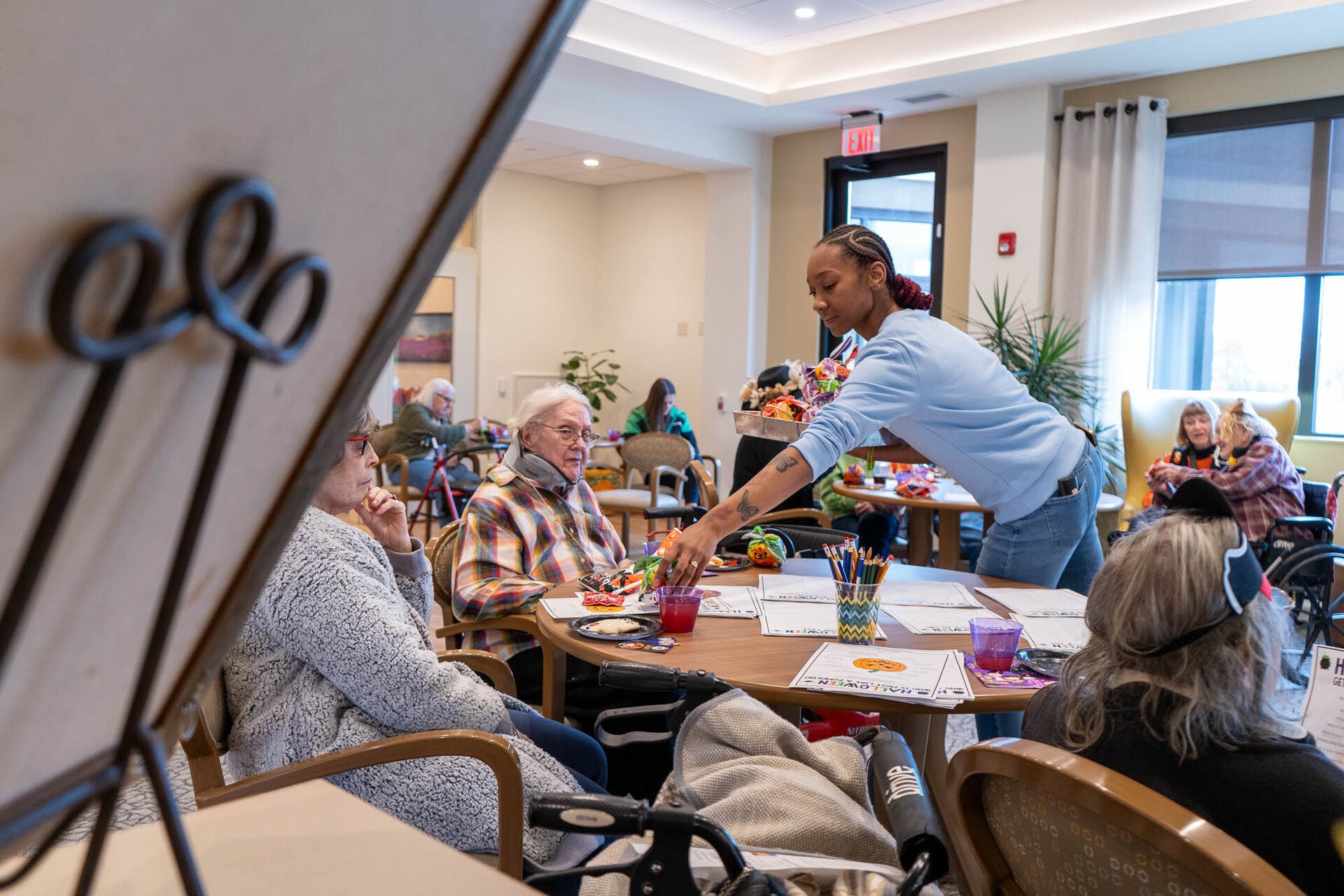 Female staff member running activities for people sitting around a table in the TLC activites room
