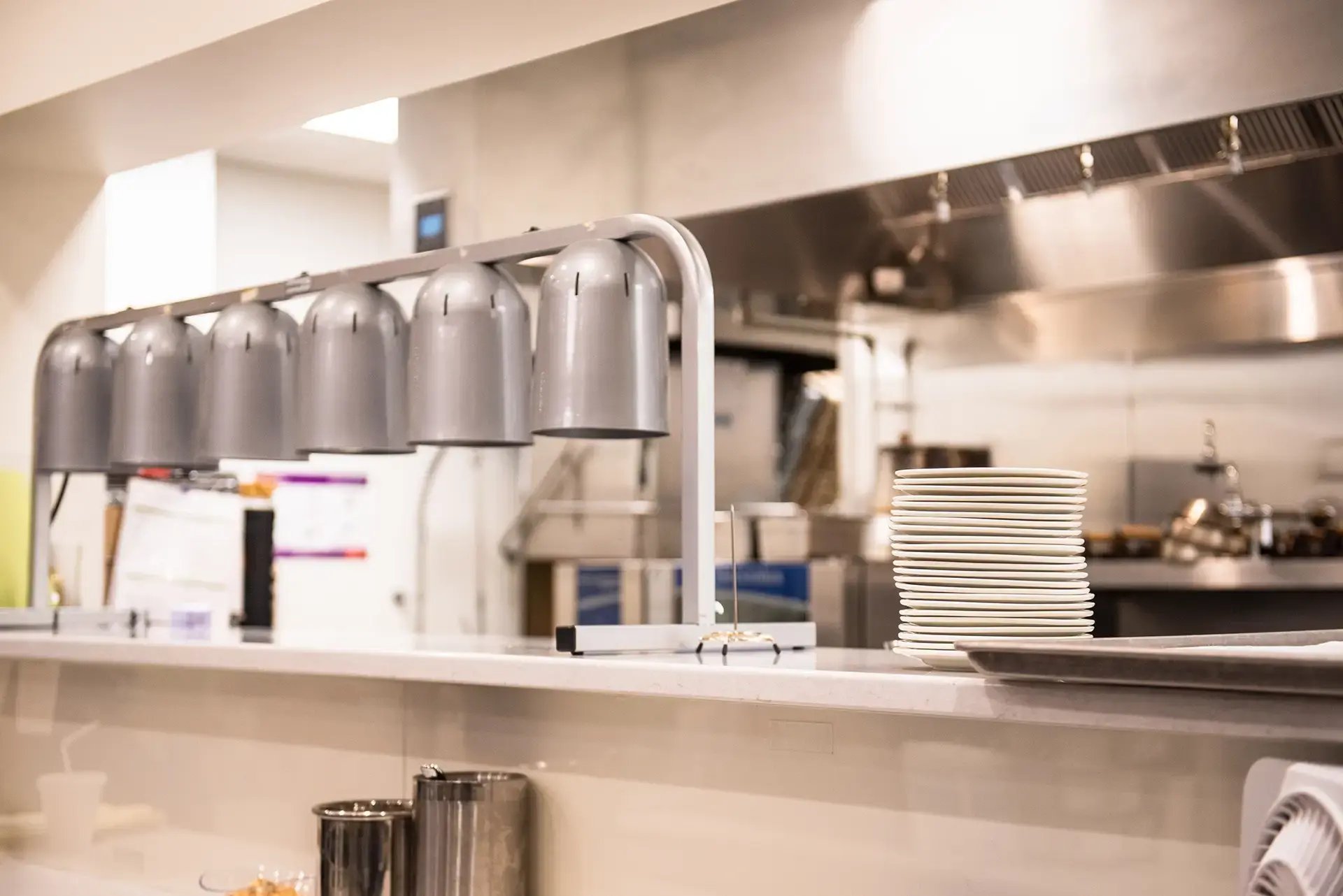 TLC cafeteria serving counter with heat lamps and a stack of plates.